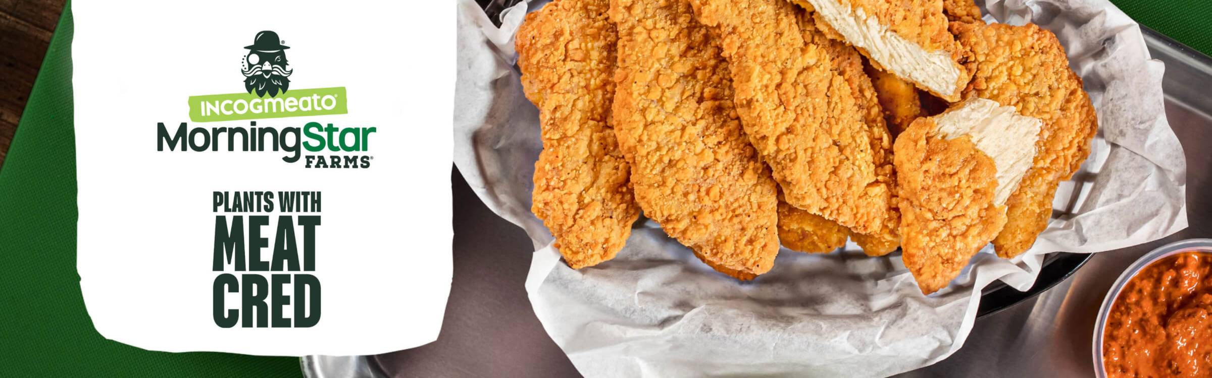 Chik'n tenders in a black basket with white wax paper and some orange colored dipping sauce on the bottom right