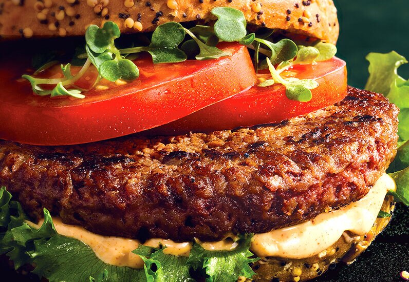 close up a plant based burger with fresh lettuce and tomotoes between black and white seasme buns