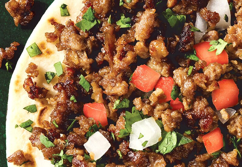 close up of a plant based grounded pork with tomatoes, onions and cilantro on a tortilla