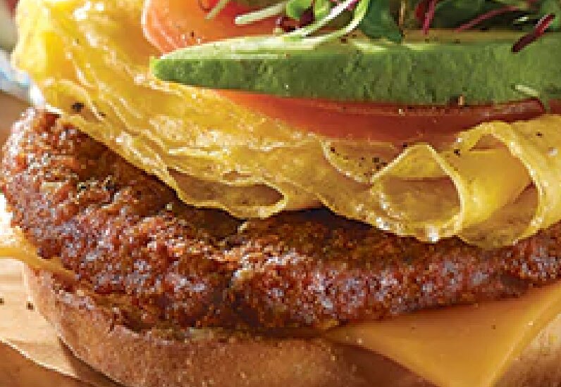 close up of a breakfast patty with cheese, bean sprouts, layered scrambled egg, lettuce, avocado and tomatoes