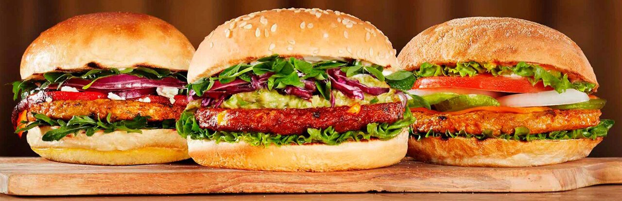 close up of three different flavored plant based hamburgers placed on a paddle wooden board