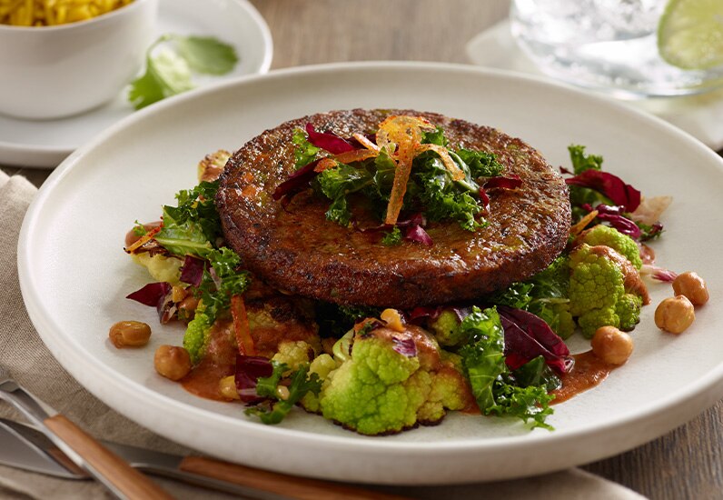 close up a Morningstar <sup>®</sup>plant-based royal thai veggie burger with visible veggies like green peas, red and green bell peppers, kale, broccoli, and more.